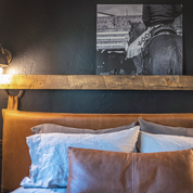 Full-grain brown leather wall-mounted headboard with topstitching, styled on a queen bed in a farmhouse design