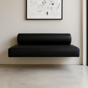 Modern black leather floating bench with cylindrical bolster backrest, wall-mounted under abstract black and white artwork in a minimalist interior