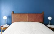 leather wall-mounted headboard with topstitching, styled on a queen bed in a modern space-saving design