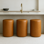 brown Modern round bar stool in full-grain leather with minimalist cylindrical shape placed in a neutral-toned luxury kitchen