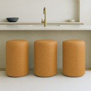 Modern round bar stool in full-grain leather with minimalist cylindrical shape placed in a neutral-toned luxury kitchen